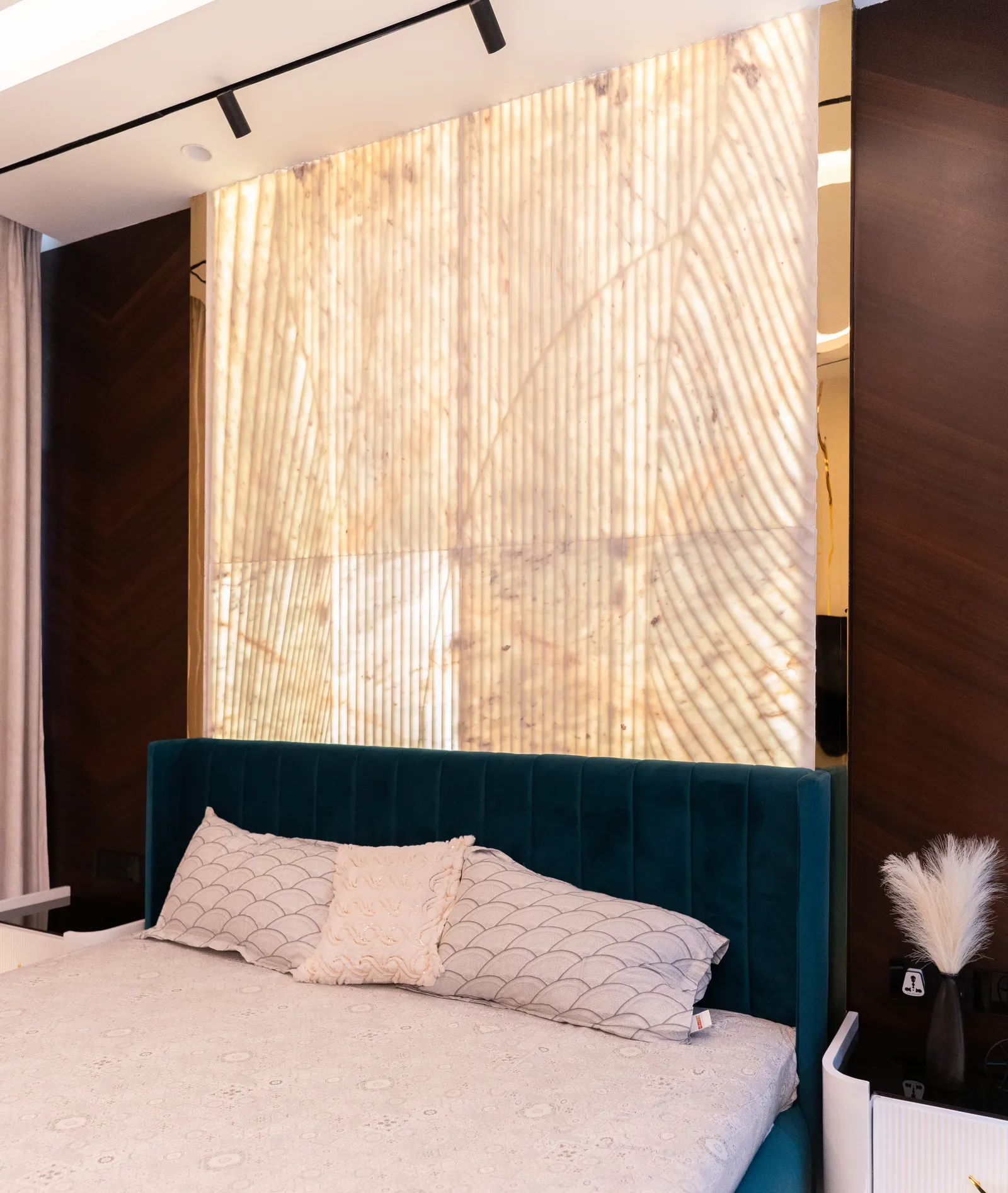 Backlit onyx feature wall behind a teal upholstered bed — Abhishek's Residence